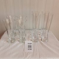 Full set of 8 specialty beer glasses, 4 tall and 4 short, arranged in two rows on a white cloth background.