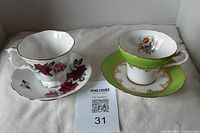 Two tea cups with saucers, one Royal Stafford with pink roses, one Royal Albert with green band and floral cluster.
