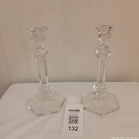 Two clear crystal candlesticks with hexagonal bases placed side by side on a white surface against a plain wall.
