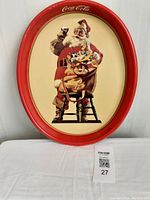 Front view showing the oval metal plater with a red rim and Santa Claus holding a glass of Coke, sitting on a chair with a sack of toys.