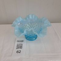 Front view of the blue opalescent hobnail glass bowl with ruffled crimped edge on a white surface.