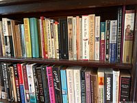 Wide view of upper shelf of books showing a variety of novels and nonfiction volumes, mostly in good condition.