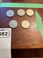 Five 1968 and 1969 Canadian silver dollar coins on a wooden surface with some green tape around, showing the reverse side with the voyageur canoe design.