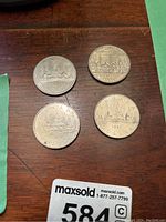 Four silver Canadian dollar coins laid on wooden surface: one 1867 Confederation coin, three 1980 Voyageur design coins.