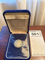 Coin in plastic sleeve displayed inside blue velvet box with certificate visible