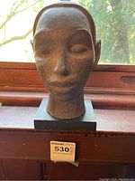 Front view of the clay bust sculpture placed on a window ledge, showing the face and base