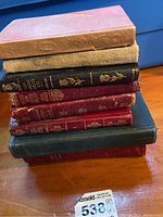Stack of seven assorted older collectible books in various colors and conditions.