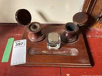 Overall view of the teak wood ink well set with two wooden wells and glass inserts, showing hinged lid open on one well and surface wear on the wood.