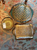 Top view of three Italian Florentine trays on patterned rug showing distinct sizes, shapes and gold painted designs