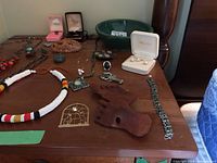 View of various necklaces, pendants, rings, bracelet, decorative pin, and green bowl on table surface
