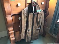 Front view of brown leather coat hanging in front of wooden dresser
