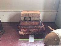 Stack of six old books showing spine wear and discoloration, placed on wooden floor