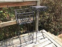 Two metal plant stands on a wooden porch railing and floor, showing overall structure and wear