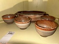 Front angled view of one smaller bowl with the casserole bowl and other smaller bowls in the background, showing glaze color and texture.