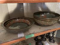 Two pottery pieces on a wooden shelf: a large bowl on the right and a plate with two handles on the left.