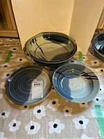 Three pottery bowls arranged on a floral patterned cloth, showing variation in size, color and brush stroke pattern. Crazing visible on bowls.