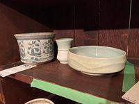 Front view photo showing three pottery items on shelf: decorative planter pot, small cup, shallow bowl