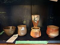Overview of four small pottery cups and one tall cup with various earthy glazes and designs