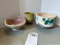 Photo showing the three pottery pieces: pink shell-shaped bowl, yellow textured cup, and white bowl with green patterns