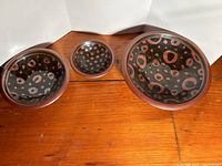 Three ceramic bowls arranged side by side showing the interior patterned designs in dark glaze with red circular spots