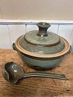 View of the soup tureen with lid and ladle on wooden surface showing glaze texture and shape.