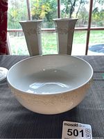 Photo showing one Wedgwood white embossed mixing bowl and two matching white embossed vases on a table near a window.