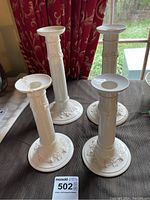 Four white Wedgwood candlesticks positioned together showing embossed floral decorations on base and column.