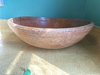 Side view of large wooden bowl showing worn edges and exterior surface.