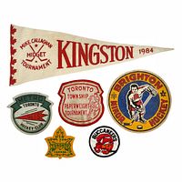 Photo showing 1 large white felt pennant with red lettering and 5 colorful embroidered felt patches related to hockey.