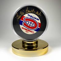 Front view of the autographed puck displayed in its transparent case on a gold-tone stand