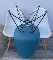 Top view of 2 white chairs and blue chair stacked on each other showing black metal wire support frames and wooden legs.