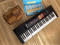 Three musical instruments: Yamaha keyboard, glockenspiel, and organic drum arranged side by side on wooden floor