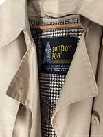 Close-up photo of London Fog trench coat label showing brand and checkered lining, proving vintage and size 14.