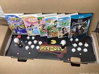 Six Nintendo Wii and Wii U game cases displayed on a Pac-Man arcade game controller station.