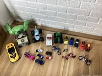 View of assorted toy vehicles and plush Hulk toy lined up on the floor including cars, trucks, motorcycles, and a large green tractor.