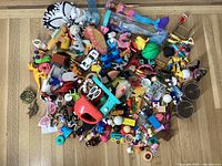 Top-down view showing a large assortment of small toys, figurines, toy vehicles, miniatures, and accessories in mixed colors and types.