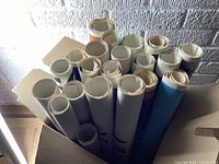 Box filled with 26 rolled vintage travel posters tightly packed together.