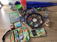 Overview photo of the entire Disney mix lot arranged on a wooden surface including tray, bags, books, keychains, necklaces, umbrellas, figurines and tumblers.