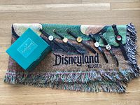 The lot laid out showing six Disneyland watches on black bands, a green box labeled 'Classics Walt Disney Collection,' and folded Disneyland Resort throw blanket with fringed edges.