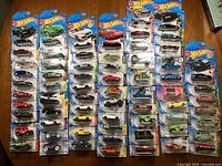 67 Hot Wheels new in box die-cast toy cars arranged on a table in multiple rows showing a range of different car models and colors.