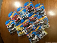 Overview of all 13 Hot Wheels trucks and vehicles in original packaging laid out on a wooden surface.