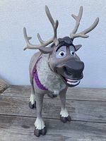 Front view of talking Sven figurine showing facial features, purple fabric collar, and antlers with one antler slightly out of place.