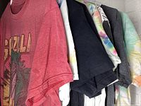 Seven assorted L/XL t-shirts arranged on hangers showing various colors and graphics including Godzilla print and others.