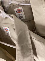Close-up of Dickies brand tags on beige shirts size 2XL, cotton blend fabric.