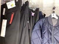 View of dark-colored dress pants on hanger with visible Calvin Klein brand tag and price sticker, along with the edge of a navy blue quilted jacket.