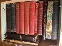 Top-down view of 15 vintage books tightly packed in a box, highlighting seven Rudyard Kipling hardcovers which are mostly red or dark leather-bound, one with a detached cover (Kim), alongside other vintage titles with varied cover colors and dust jackets.