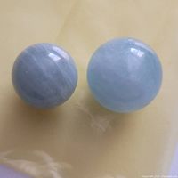 Two aquamarine marbles with one lighter and translucent, the other smaller and banded, on a yellow background.