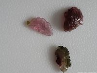 Three small bi-colour tourmaline carvings shaped like fish or leaves on a white textured background.