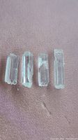 Four raw aquamarine crystals laid side by side on a pink fabric surface showing their clear and toothy edges.