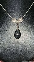 Close-up of necklace with dark smoky crystal teardrop pendant and two disco ball beads on a thin silver chain.